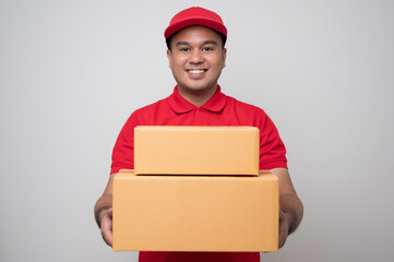 Young smiling asian delivery man in red uniform holding box parcel cardboard giving to customer standing on isolated white background..