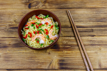 Bowl of instant Chinese noodles with shrimps, green onion and red hot chilli peppers on wooden table. Top view