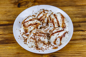 Vanilla ice cream with chocolate topping in white plate on a wooden table