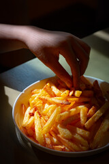 A hand picking up French fries from white dish on the table.