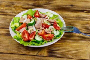 Tasty tuna salad with lettuce and fresh vegetables on wooden table