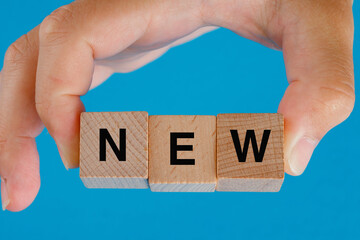 Business idea concept on blue background side view. hand holding wooden cubes with word new.