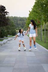 Obraz premium happy mother and her little daughter rollerskating in summer park. family have fun