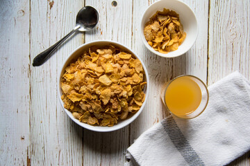 Top view of a bowl of cereal corn flakes and fruit juice on a background.