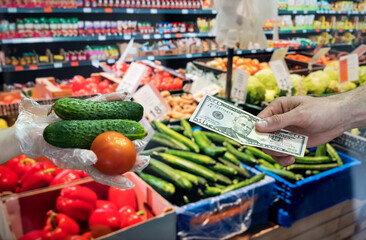 seller in gloves sells fresh vegetables. man gives dollars for groceries in the supermarket.