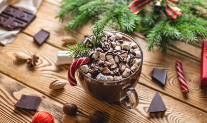 Obraz na płótnie Canvas A cup of aromatic tasty hot chocolate with marshmallows decorated with red candy on a wooden table surrounded by Christmas accessories. Concept of a festive atmosphere and cozy New Year mood
