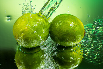 two whole limes with splashing water on gradient background