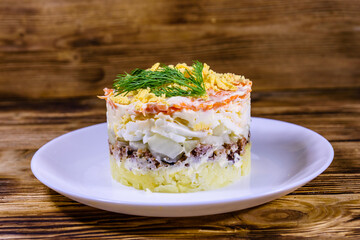 Plate with traditional russian salad Mimosa on a wooden table. Layered salad with potatoes, sardine, cheese, carrot, eggs and mayonnaise