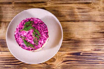 Ceramic plate with russian traditional new year salad herring under fur coat (shuba) and on rustic wooden table. Top view