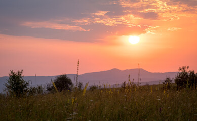 The sun rises against the background of the mountains. Green grass in the morning sun
