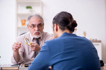 Young man visiting old male jeweler
