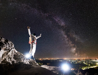 Astronaut raising arms while standing on rocky mountain with fantastic starry sky with Milky way on...
