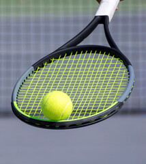 Tennis ball on tennis racket and blurred tennis court in background. Sport game and active healthy lifestyle concept. Close up