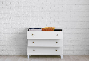 Modern chest of drawers with clothes near brick wall in room
