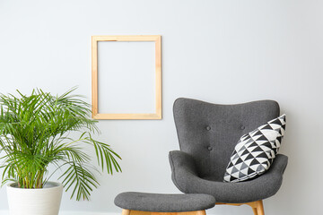Stylish armchair and ottoman with houseplant near light wall in room