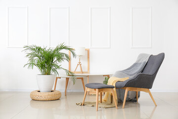 Stylish armchair and ottoman with table and houseplant near light wall in room