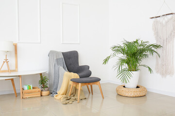 Stylish armchair and ottoman with table and houseplant near light wall in room