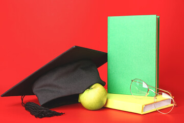 Graduation hat, eyeglasses and books on color background