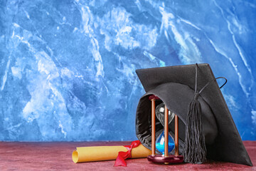 Graduation hat, diploma and hourglass on color background