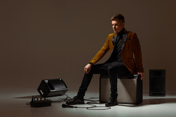 handsone singer in suit sitting on a musical column in the studio dark background