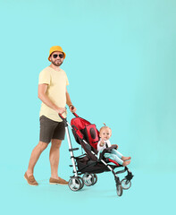 Father and his cute baby in stroller on color background