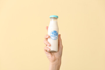 Female hand with bottle of soy milk on color background