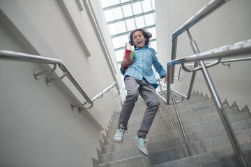 Fototapeta premium Excited schoolboy running downstairs with pile of books