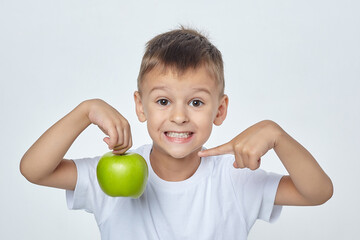 small boy with a smile holds a green Apple and points at it with his finger. photo session in the Studio on a white background