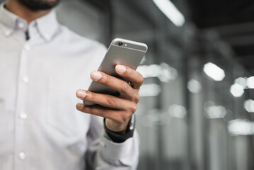 Closeup photo of male hand with smartphone at office, young man using mobile phone indoors