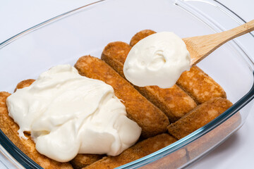 tiramisu dessert cooking - Traditional Italian Savoiardi ladyfingers Biscuits and cream in glass baking dish isolated on white with clipping path