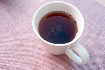Close up view of a white ceramic cup of tea on the pink tablecloth.