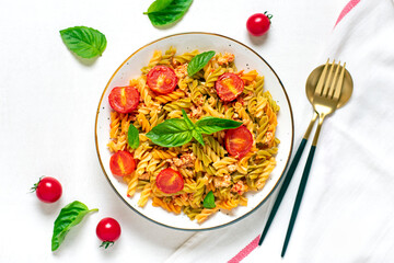 Fusilli - classic italian pasta from durum wheat with chicken meat, tomatoes cherry, basil in tomato sauce in bowl, spoon, fork on white wooden table Mediterranean cuisine Top view Flat lay