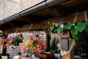 A brown letterbox under a street lamp on a wooden texture by a gazebo with hanging flower pots and tables and chairs.