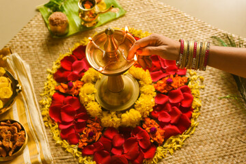 Women Lighting lamp and traditional flower bed for Onam, harvest festival of Kerala India. fresh flower carpet floral pattern made for Indian festival Vishu, dussehra, dasara, diwali celebration also.