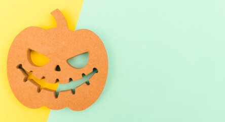 Halloween background idea.Flat lay wooden Jack o lantern spooky pumpkin on green yellow paper color background.Halloween design with copy space for text advertising.Background idea in Autumn October.
