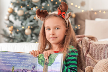 Cute little girl reading book at home on Christmas eve
