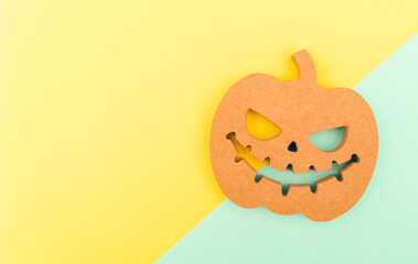 Halloween background idea.Flat lay wooden Jack o lantern spooky pumpkin on green yellow paper color background.Halloween design with copy space for text advertising.Background idea in Autumn October.
