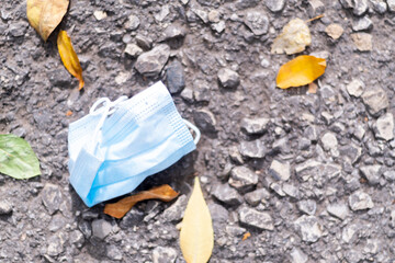 Used medical mask on the ground. Mask for protection from the flu epidemic, viruses and coronavirus. Surgical mask thrown on the ground after use. Laying among leaves and becoming trash.
