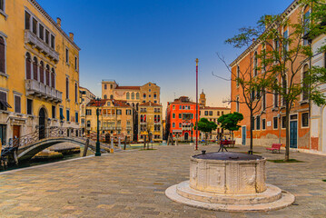 Fototapeta na wymiar Campo San Vio with Palazzo Cini and Palazzo Barbarigo palaces, stone well and bridge across narrow water canal, buildings on Grand Canal waterway in Venice historical city centre background, Italy