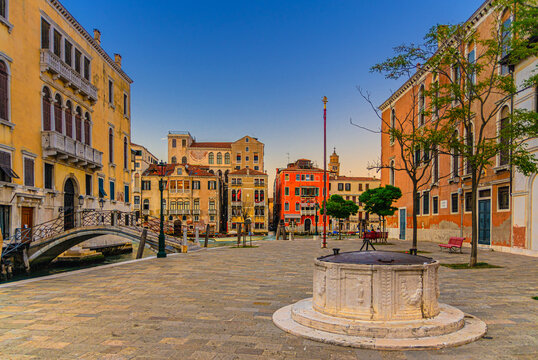 Campo San Vio with Palazzo Cini and Palazzo Barbarigo palaces, stone well and bridge across narrow water canal, buildings on Grand Canal waterway in Venice historical city centre background, Italy