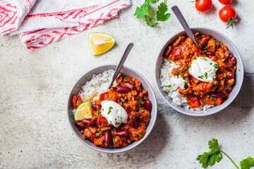 Chili con carne with rice in gray bowl, top view. Beef stew with beans in tomato sauce with sour cream and rice. Traditional Mexican food concept.