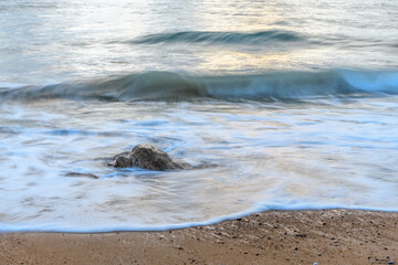 Rocks on the beach in the evening with moving water which brings an effect to the surface of the sea.