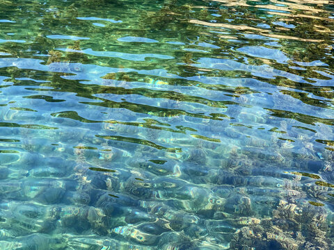 Turquoise crystal clear water in Adriatic sea. Rippled water detail background. Amazing watercolor. Pebble seabed. Water surface with sun light reflection and ripples on surface. Calm. Meditation. 