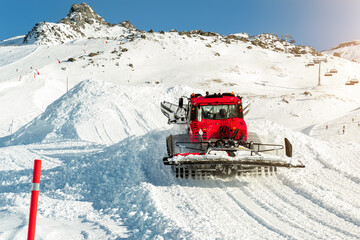 Red modern snowcat ratrack with snowplow snow grooming machine preparing ski slope piste hill at...