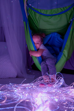 Child in therapy sensory stimulating room, snoezelen. Autistic child interacting with colored lights during therapy session.