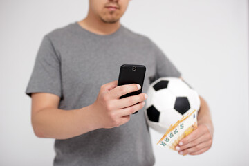 sport, online bet, success, win and money concept - young man holding smart phone, euro money and  soccer ball over grey background