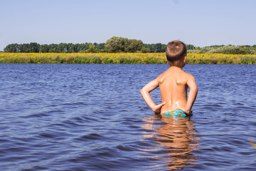 a boy stands in a river against the background of a yellow field