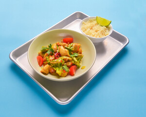 Fresh rice and chicken in gravy sauce with tomatoes, red pepper and green beans served in seperate plates on metal tray.