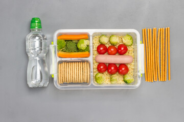 Lunch box with sausage, broccoli and tomatoes. Bottle of water and edible straw