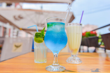 Three fresh juice drinks in tall glasses with plastic straws outside. Milkshake, blue curacao cocktail and mohito.